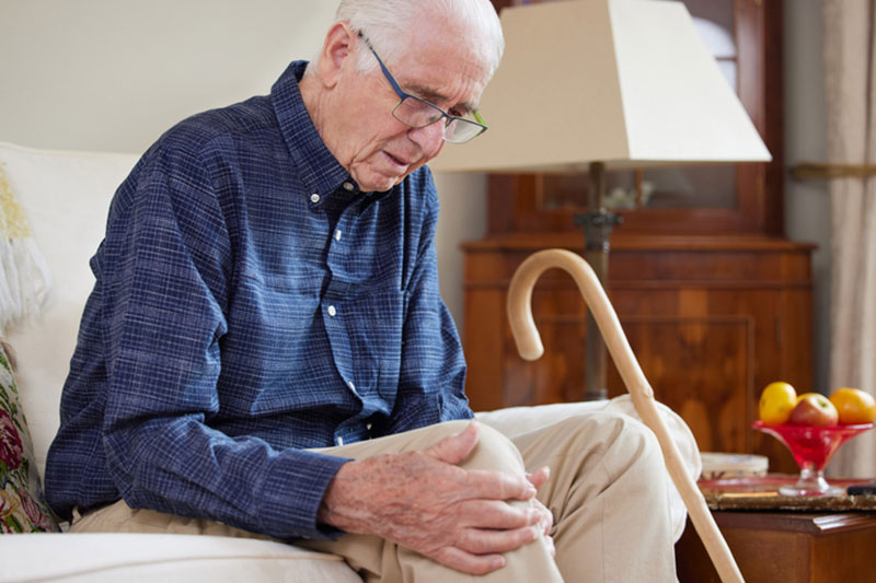 An older man rubs his sore knee before preparing for joint replacement surgery.